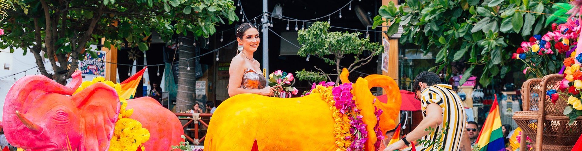 Woman in parade, seated on yellow elephant sculpture adorned with flowers